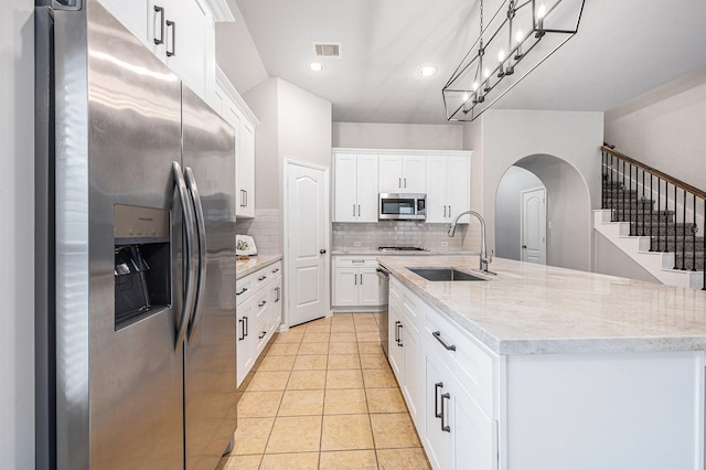 kitchen featuring stainless steel appliances, a sink, white cabinetry, and decorative light fixtures