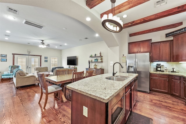 kitchen with stainless steel appliances, decorative light fixtures, beamed ceiling, light stone counters, and a kitchen island with sink