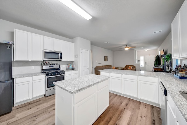 kitchen featuring ceiling fan, white cabinetry, stainless steel appliances, light stone countertops, and light hardwood / wood-style floors