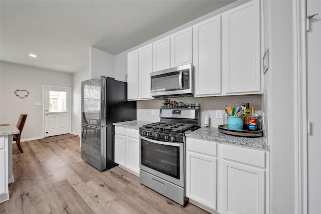 kitchen featuring white cabinetry, light stone counters, stainless steel appliances, and light wood-type flooring