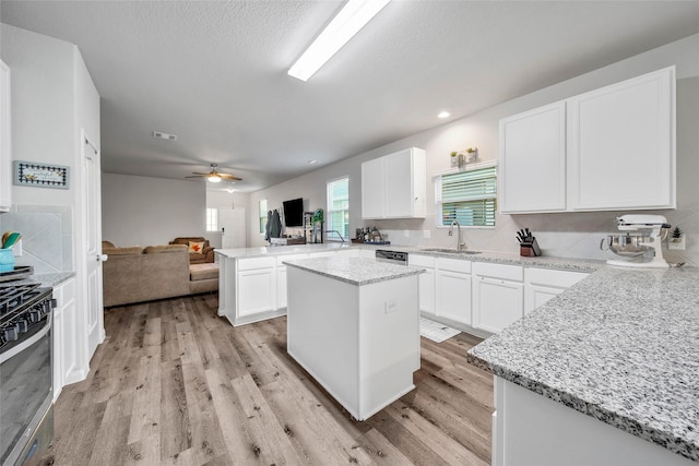 kitchen featuring sink, light stone counters, white cabinetry, a center island, and kitchen peninsula