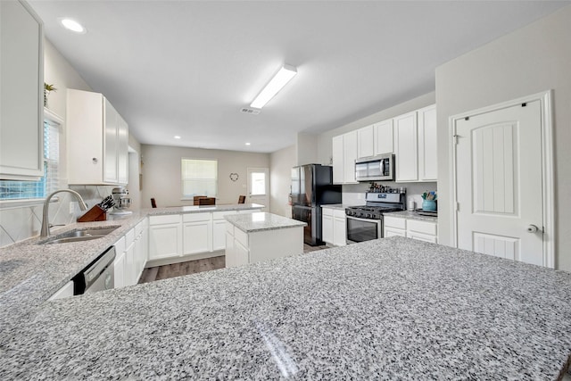 kitchen featuring sink, appliances with stainless steel finishes, kitchen peninsula, a kitchen island, and light stone countertops