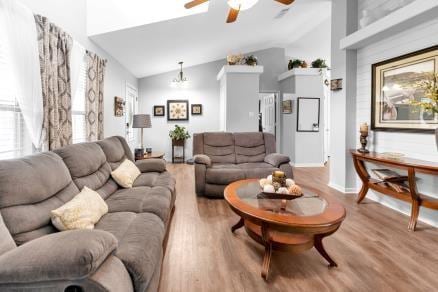 living room with ceiling fan with notable chandelier, vaulted ceiling, and wood-type flooring