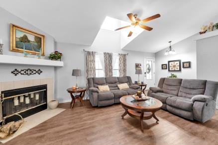 living room featuring lofted ceiling, a tiled fireplace, ceiling fan with notable chandelier, and hardwood / wood-style floors