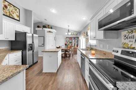 kitchen with stainless steel appliances, white cabinets, light stone counters, lofted ceiling, and a chandelier