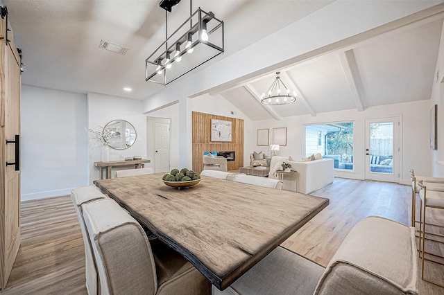 dining area featuring an inviting chandelier, lofted ceiling with beams, light wood-type flooring, and a barn door