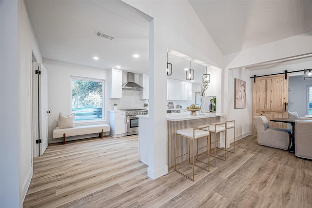 kitchen with white cabinets, high end stove, wall chimney exhaust hood, a kitchen bar, and a barn door