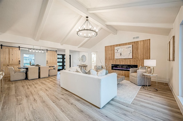 living room with an inviting chandelier, lofted ceiling with beams, light hardwood / wood-style floors, and a barn door