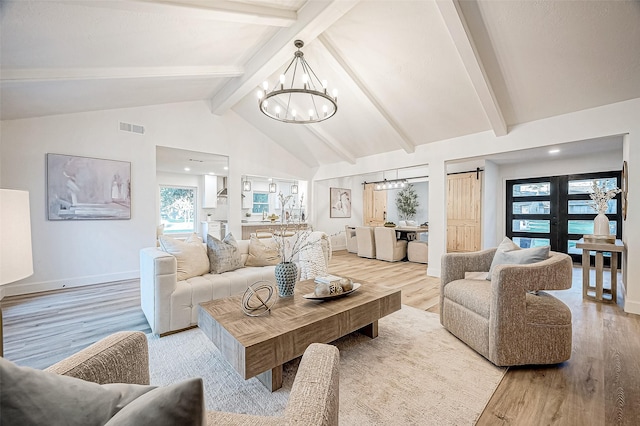 living room featuring a barn door, lofted ceiling with beams, light wood-type flooring, and a notable chandelier