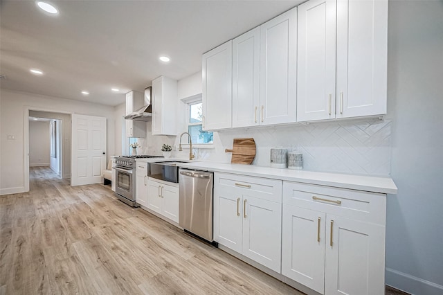 kitchen featuring stainless steel appliances, decorative backsplash, white cabinetry, and wall chimney range hood