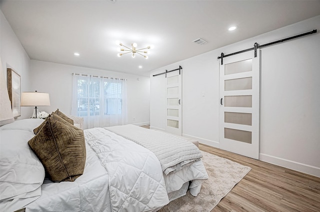 bedroom with light hardwood / wood-style floors, an inviting chandelier, and a barn door