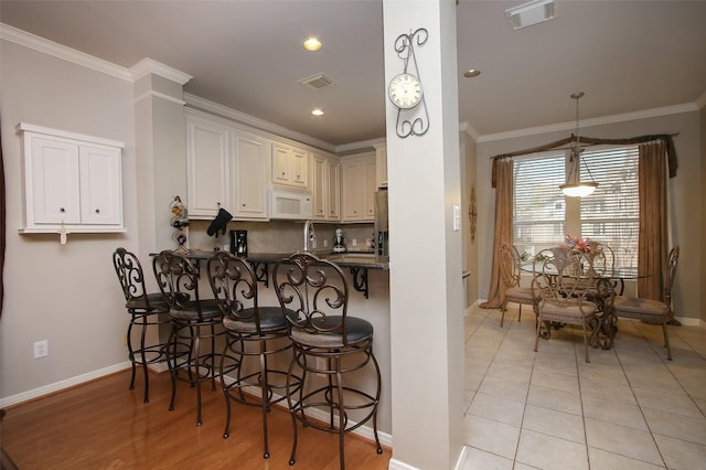 kitchen with light tile patterned flooring, a breakfast bar, hanging light fixtures, ornamental molding, and kitchen peninsula