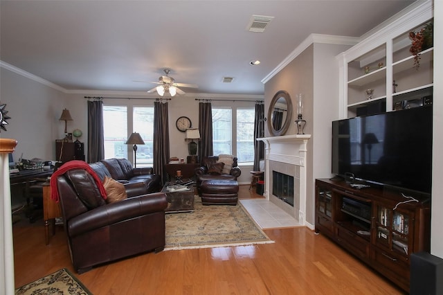 living room featuring crown molding, ceiling fan, a fireplace, and light hardwood / wood-style flooring