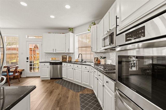 kitchen with stainless steel appliances, dark stone counters, sink, white cabinetry, and tasteful backsplash