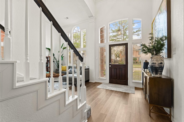 foyer entrance featuring a towering ceiling, light wood-type flooring, and crown molding