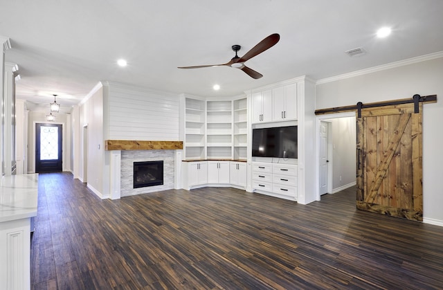 unfurnished living room with dark hardwood / wood-style floors, a barn door, ceiling fan with notable chandelier, a fireplace, and ornamental molding