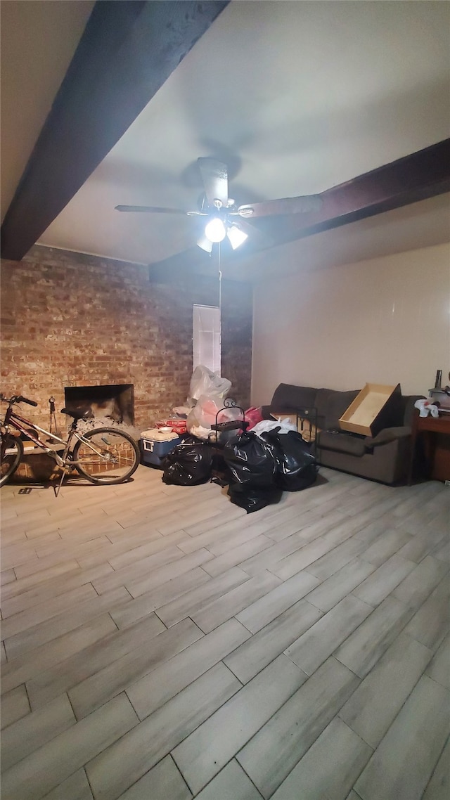 interior space featuring ceiling fan, beam ceiling, light hardwood / wood-style floors, a large fireplace, and brick wall