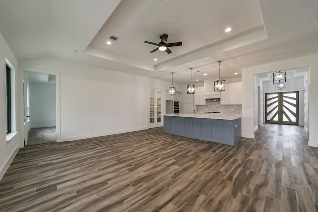 kitchen featuring white cabinets, pendant lighting, ceiling fan with notable chandelier, dark hardwood / wood-style flooring, and a kitchen island with sink