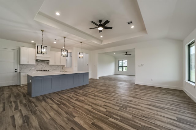 kitchen with white cabinets, a raised ceiling, pendant lighting, ceiling fan with notable chandelier, and a kitchen island with sink