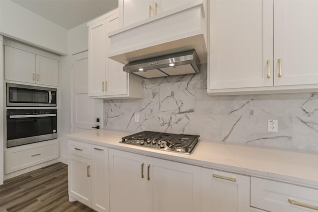 kitchen with appliances with stainless steel finishes, premium range hood, dark hardwood / wood-style flooring, white cabinets, and backsplash