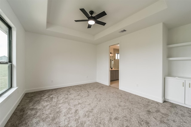 spare room with built in features, a tray ceiling, a wealth of natural light, and light carpet