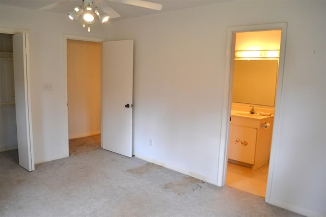 unfurnished bedroom featuring sink, a closet, ceiling fan, light colored carpet, and ensuite bathroom