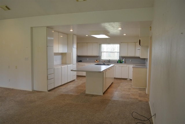 kitchen with white cabinets, sink, light colored carpet, and a kitchen island