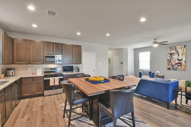 kitchen with light stone counters, ceiling fan, light wood-type flooring, backsplash, and appliances with stainless steel finishes