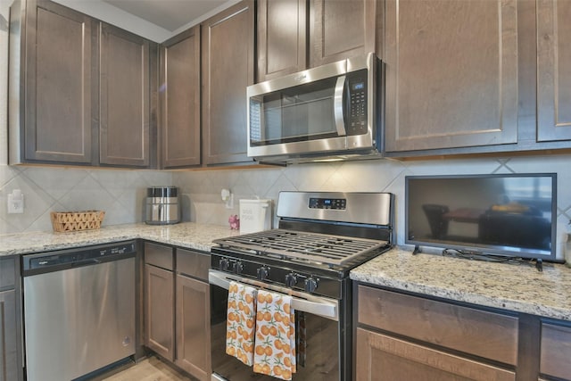 kitchen with stainless steel appliances, dark brown cabinets, backsplash, and light stone countertops