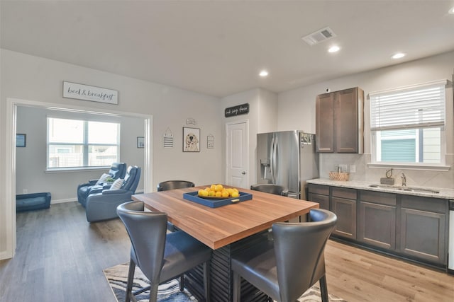 kitchen featuring sink, light stone counters, light wood-type flooring, dark brown cabinets, and stainless steel refrigerator with ice dispenser