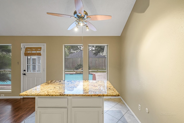 kitchen with ceiling fan, white cabinetry, light stone counters, and a kitchen island