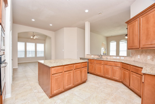 kitchen featuring light stone counters, sink, backsplash, and a kitchen island