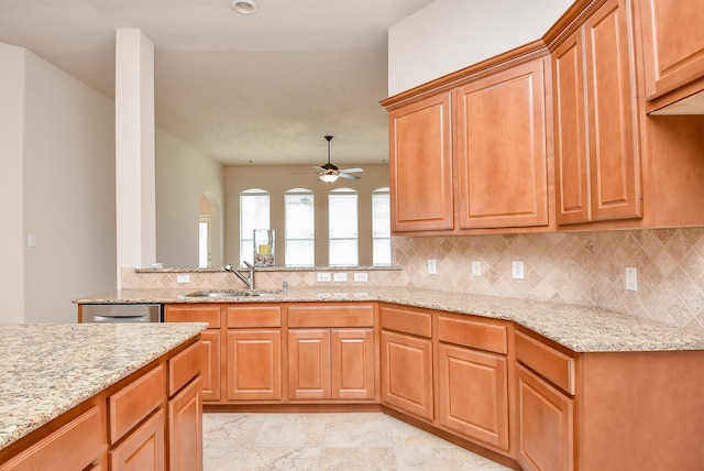 kitchen featuring ceiling fan, sink, light stone counters, and decorative backsplash