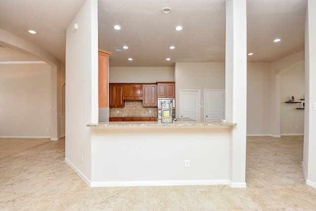 kitchen with stainless steel microwave, light stone counters, kitchen peninsula, and tasteful backsplash