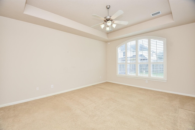 unfurnished room with ceiling fan, a tray ceiling, and light carpet