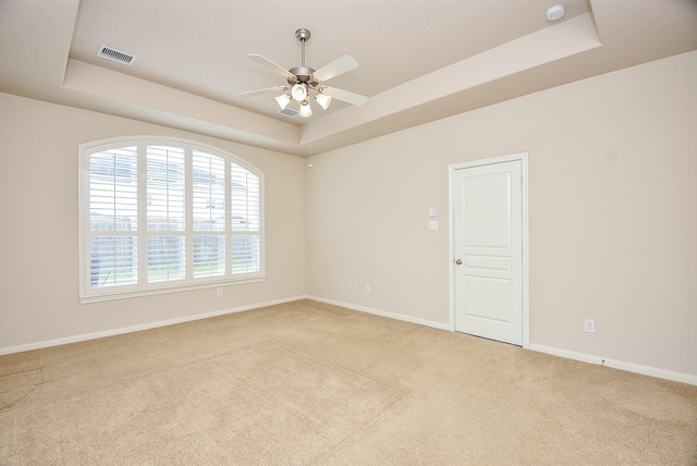 unfurnished room with ceiling fan, light colored carpet, and a tray ceiling