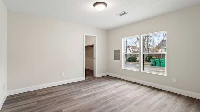 unfurnished bedroom featuring electric panel, a spacious closet, hardwood / wood-style floors, and a closet