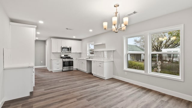 kitchen featuring stainless steel appliances, pendant lighting, sink, white cabinetry, and an inviting chandelier