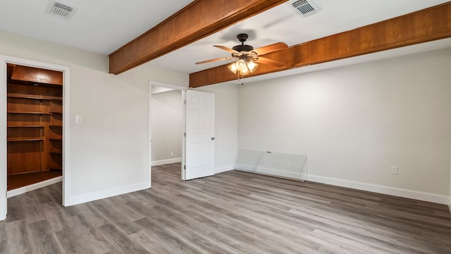 unfurnished bedroom with a closet, beamed ceiling, ceiling fan, hardwood / wood-style flooring, and a walk in closet