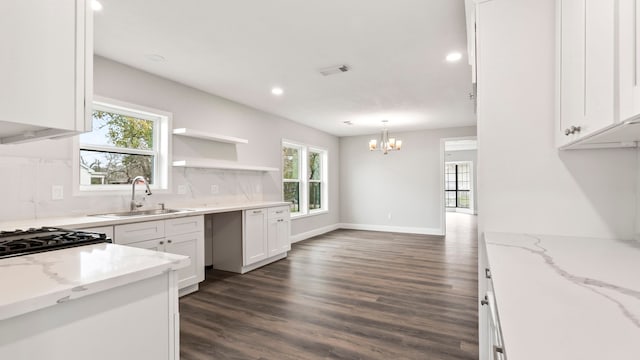 kitchen with white cabinets, hanging light fixtures, light stone counters, dark hardwood / wood-style floors, and sink