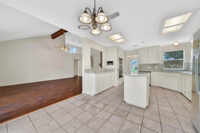 kitchen featuring light tile patterned floors, decorative backsplash, ceiling fan with notable chandelier, white cabinets, and a center island