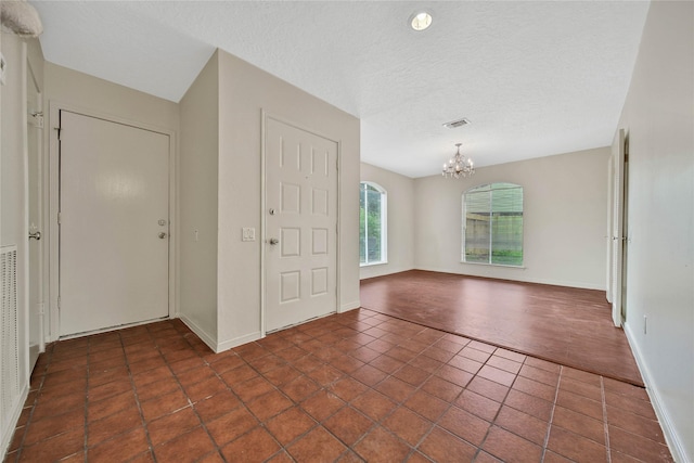 entryway with a notable chandelier, dark tile patterned flooring, and a textured ceiling