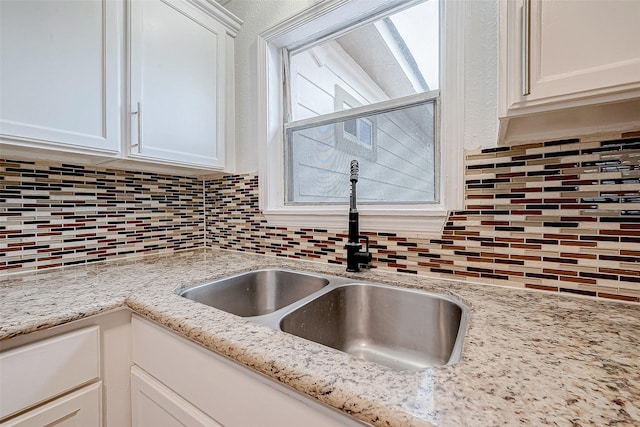 interior details featuring light stone counters, white cabinets, decorative backsplash, and sink