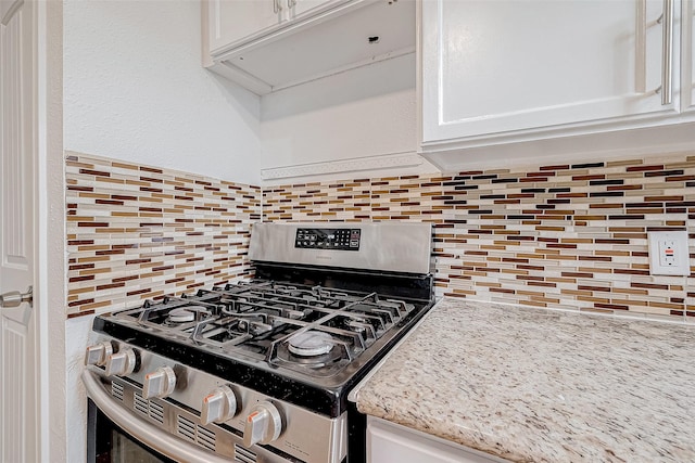 kitchen featuring light stone countertops, stainless steel gas range, white cabinetry, and decorative backsplash