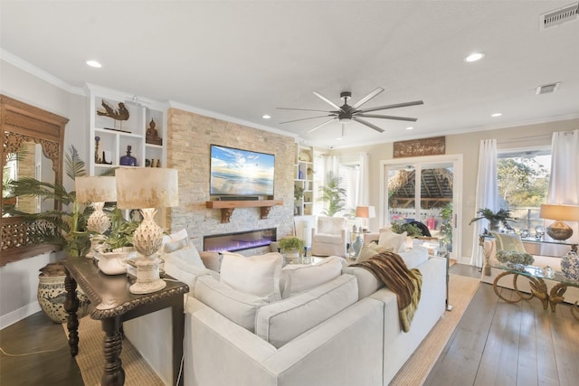 living room with ceiling fan, a fireplace, wood-type flooring, crown molding, and built in features