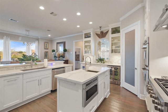 kitchen with white cabinetry, appliances with stainless steel finishes, a kitchen island with sink, wine cooler, and sink