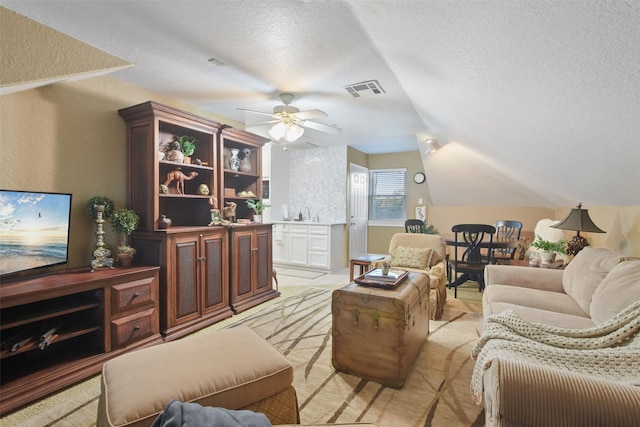 living room featuring ceiling fan, vaulted ceiling, and a textured ceiling