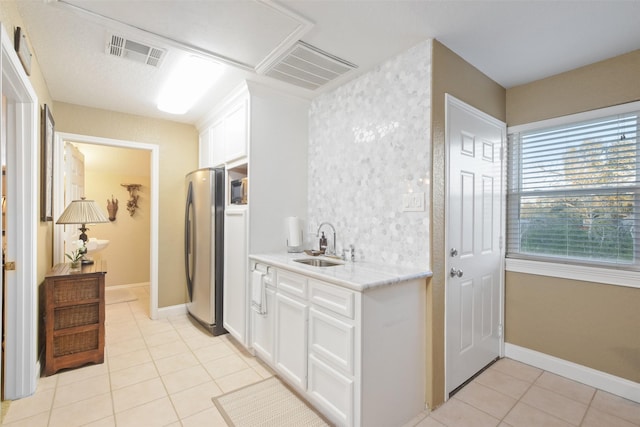 kitchen with light tile patterned floors, sink, white cabinets, and stainless steel refrigerator