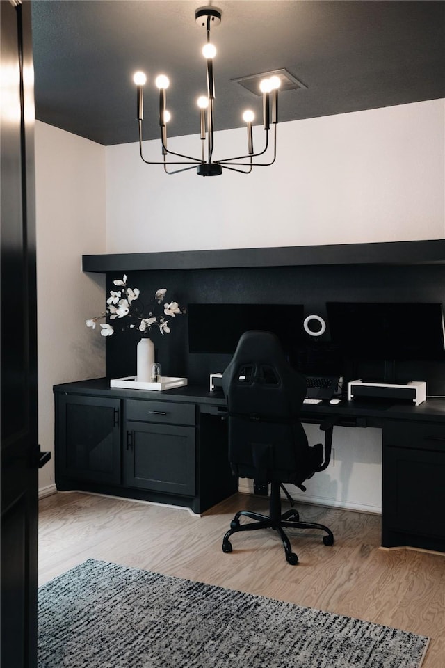 home office with light hardwood / wood-style floors, an inviting chandelier, and built in desk