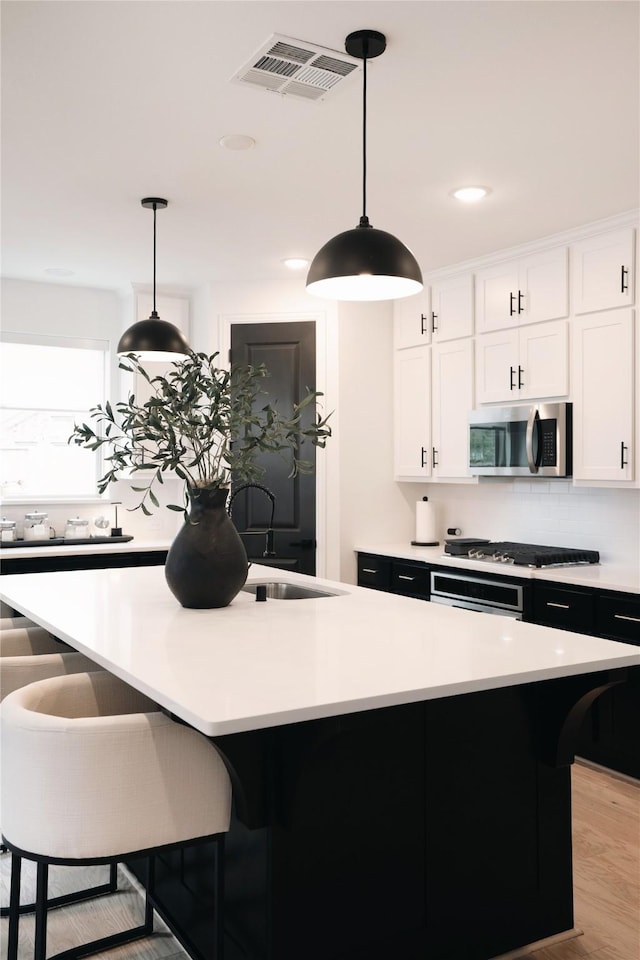 kitchen with pendant lighting, stainless steel appliances, a kitchen island with sink, white cabinets, and sink